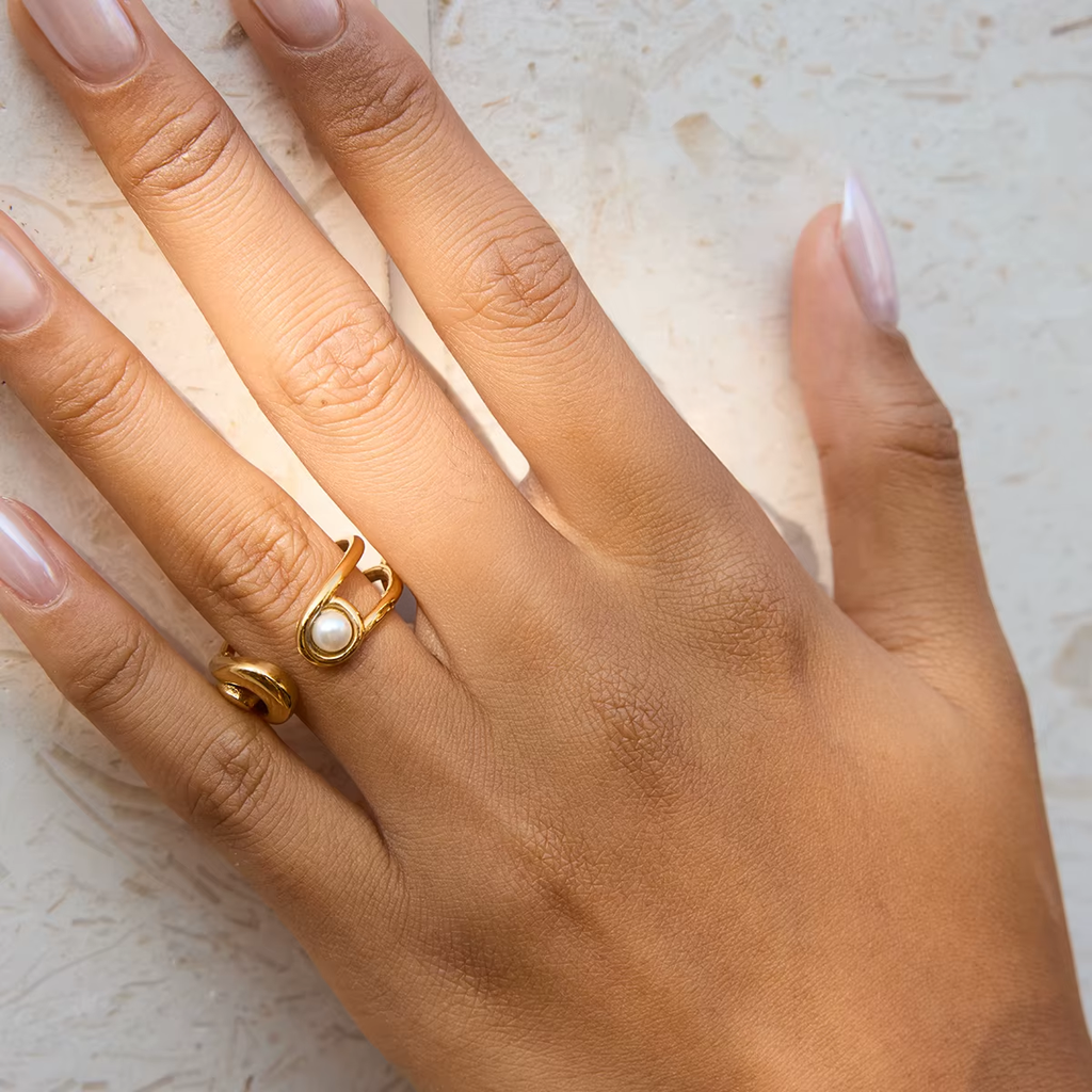 Hand wearing a gold ring with a pearl on a light background