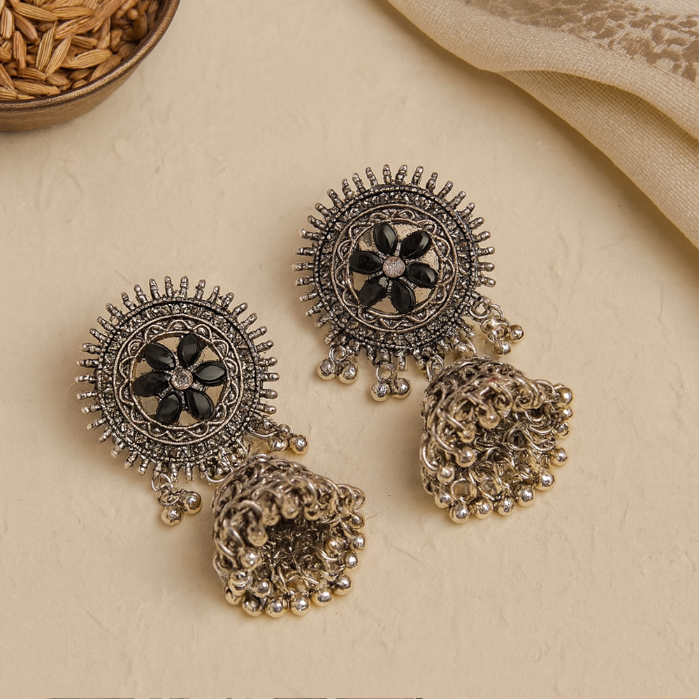 Ornate silver earrings with black accents on a beige surface