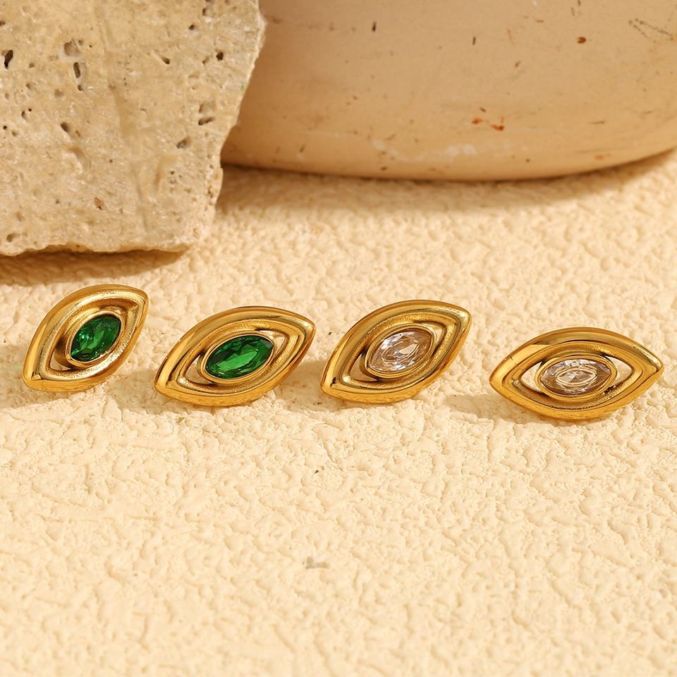 Gold earrings for women with green and clear gemstones on a beige surface