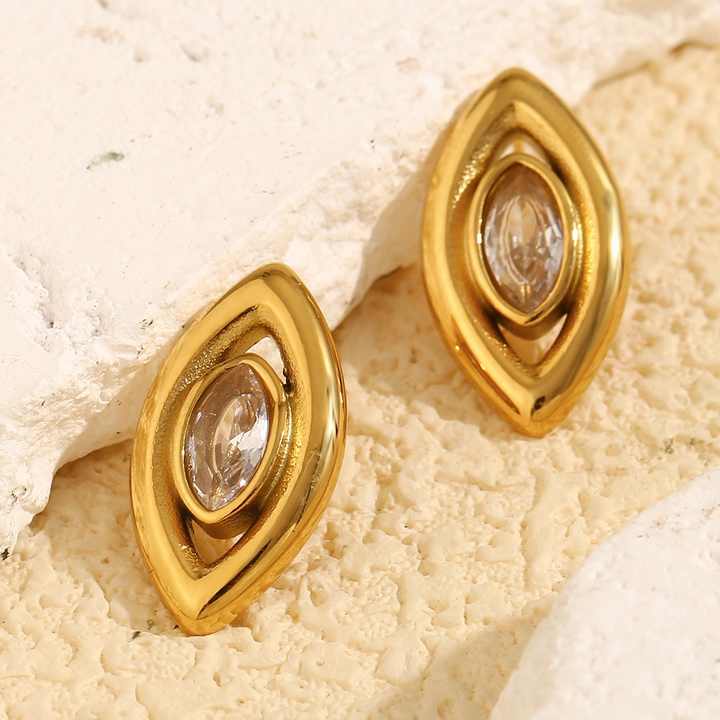 Gold earrings with a central gemstone on a textured beige surface