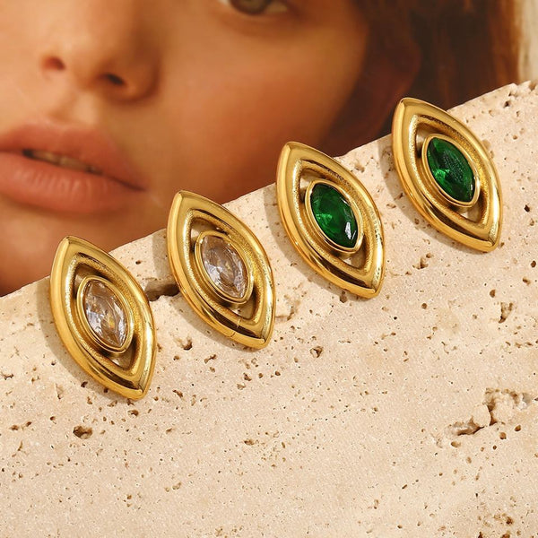 Gold earrings for women with green and clear gemstones on a textured surface